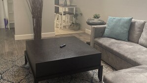 Una sala de estar con una mesa baja oscura, un sofá gris y un tapete estampado.