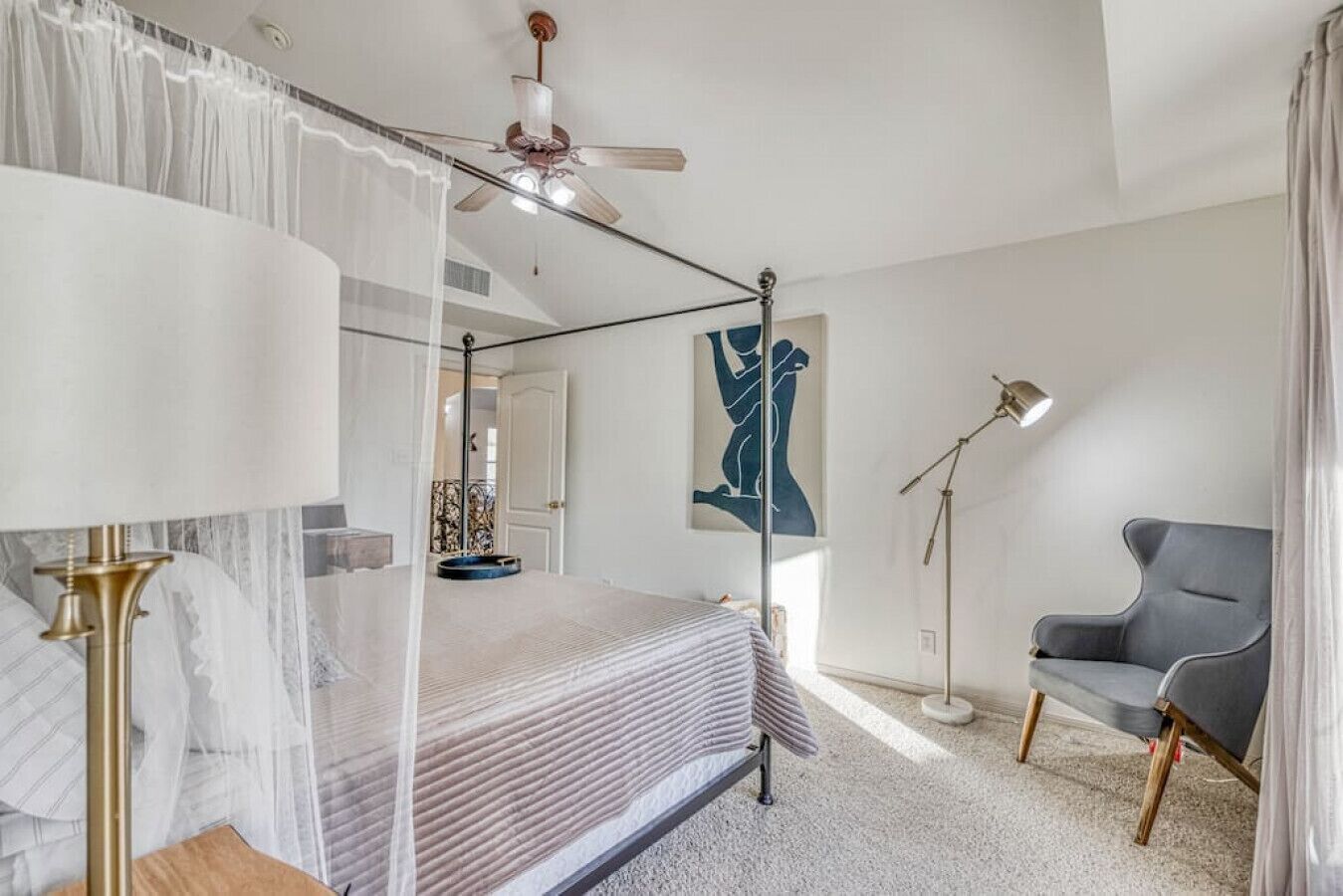 Une chambre à coucher avec un lit, une lampe sur pied, une chaise, un ventilateur de plafond et un tableau accroché au mur.