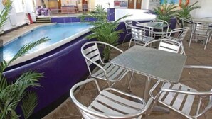 Uma área de piscina interna com trampolim, cercada por cadeiras e mesas de metal.