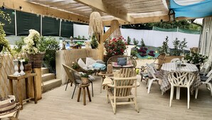 A covered outdoor patio area with wicker furniture, a table, and various potted plants.