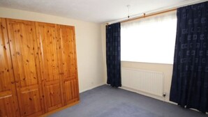 Une pièce avec une grande armoire en bois, un radiateur et une fenêtre ornée de rideaux foncés.