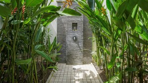 A stone wall with a small window and a water feature in a lush garden.