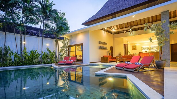 A modern resort with a swimming pool, red lounge chairs, and a well-lit interior.