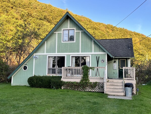 A green two-story house with a porch, a small deck, and a front door. - Creekside Chalet (swain)