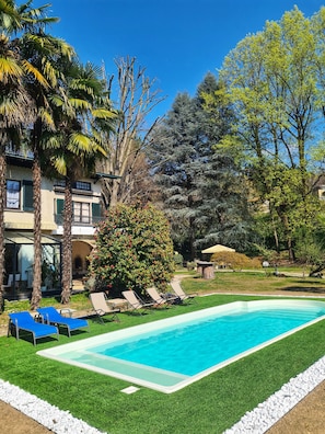Piscina com água azul cristalina, rodeada por grama sintética e algumas espreguiçadeiras.