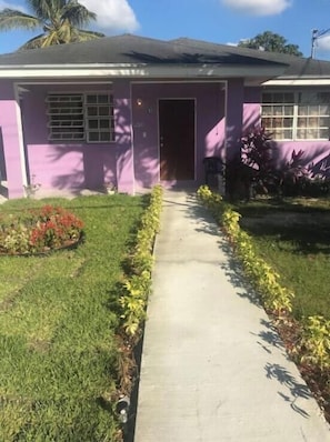 Uma casa térrea com porta de entrada, um pequeno alpendre e um caminho que leva à entrada.