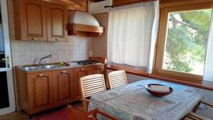 A compact kitchen with wooden cabinets, a gas stove, and a window with a view of trees. - Spectacular Sea View Sardinia! 300m From The Sea! (Quartu Sant'Elena)