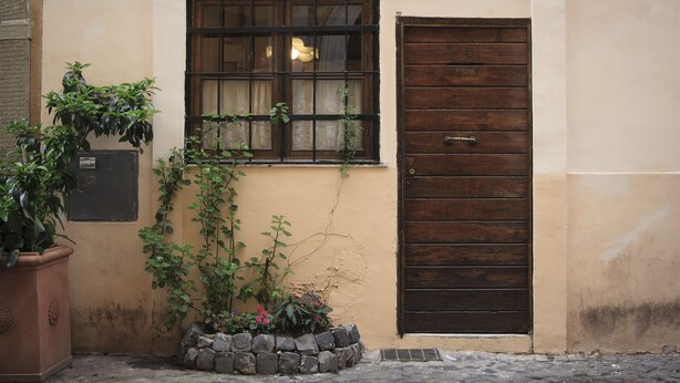 A narrow alley with a door and window, surrounded by plants and a stone wall. - Trastevere, Pretty,central,economic (Rome)