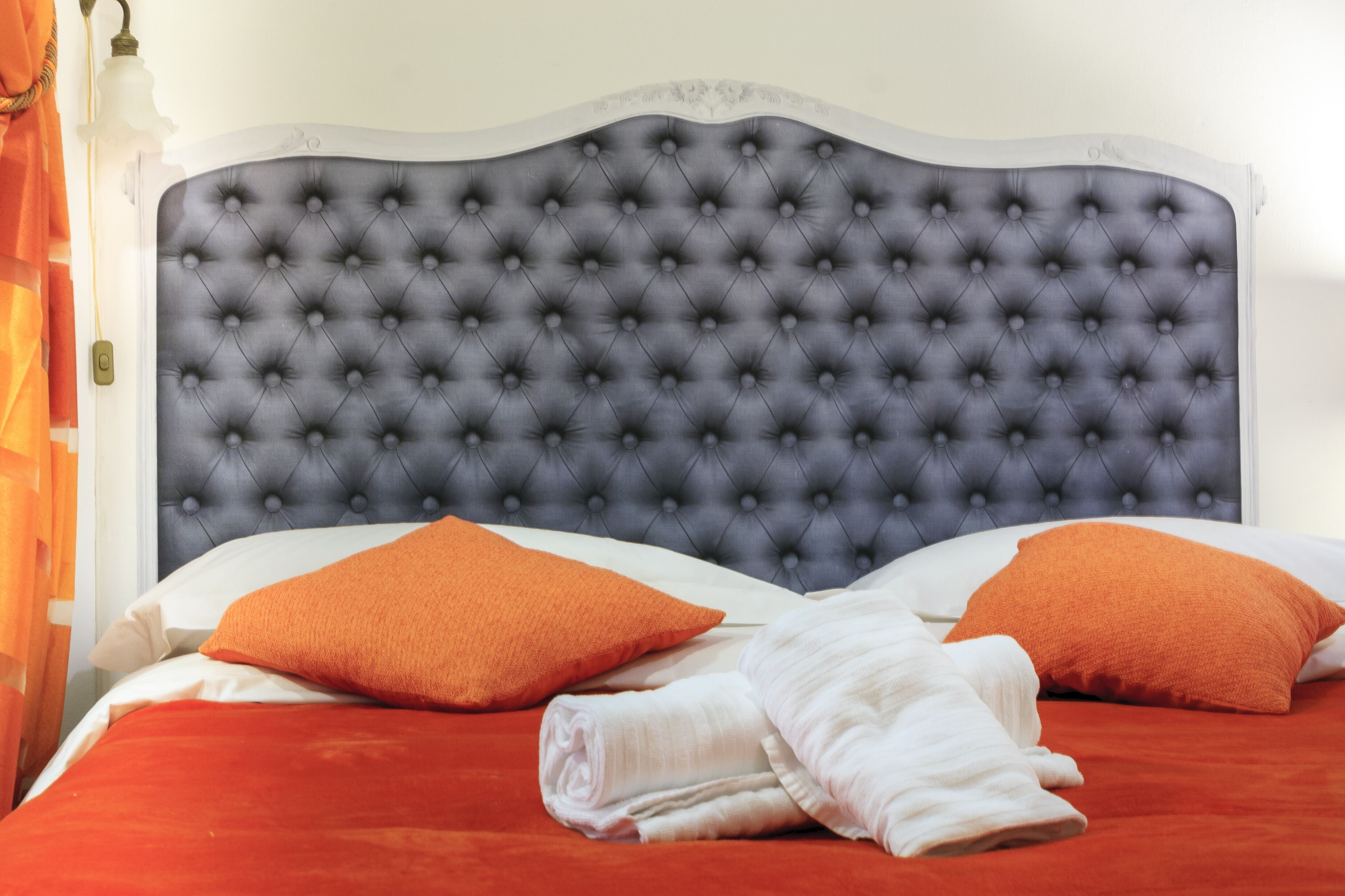 A bed with a tufted headboard, two orange pillows, and a red bedspread.