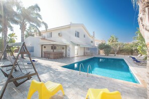 Piscina com área de terraço, balanço e uma casa ao fundo.