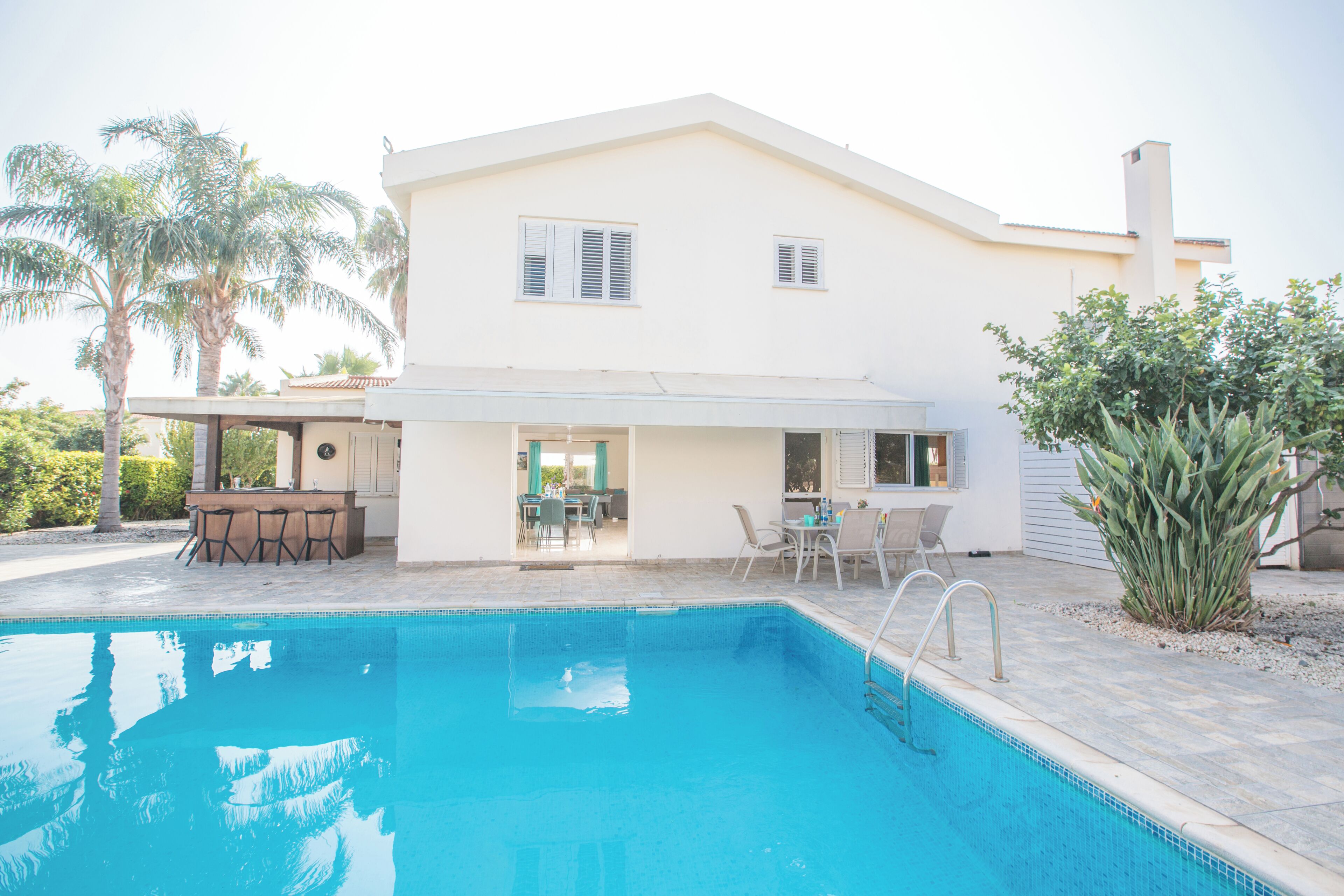 A two-story house with a swimming pool, outdoor seating, and palm trees.