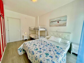 Un dormitorio con literas, una cama individual, una mesita de noche, un cuadro y una puerta con cortinas rojas.