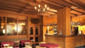 Ein gemütliches Restaurant mit Holzeinrichtung, einer Bar mit Flaschen und Tischen, die mit roten Tischdecken gedeckt sind.