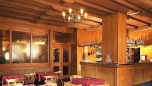Un restaurante acogedor con interiores de madera, una zona de bar con botellas y mesas dispuestas con manteles rojos.