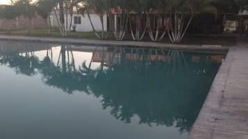 Una piscina rectangular que refleja claramente árboles y un edificio blanco al fondo.