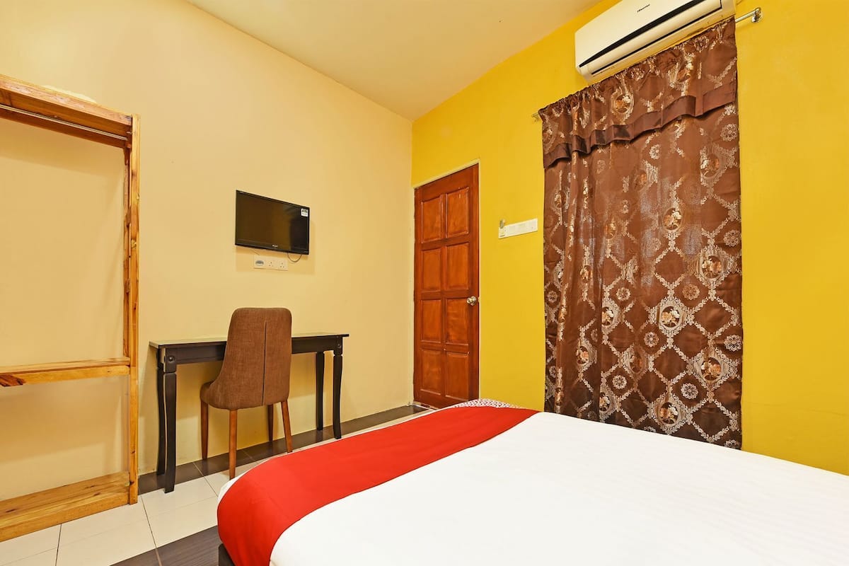 A hotel room with a bed, a desk, a chair, a television, and a wardrobe.