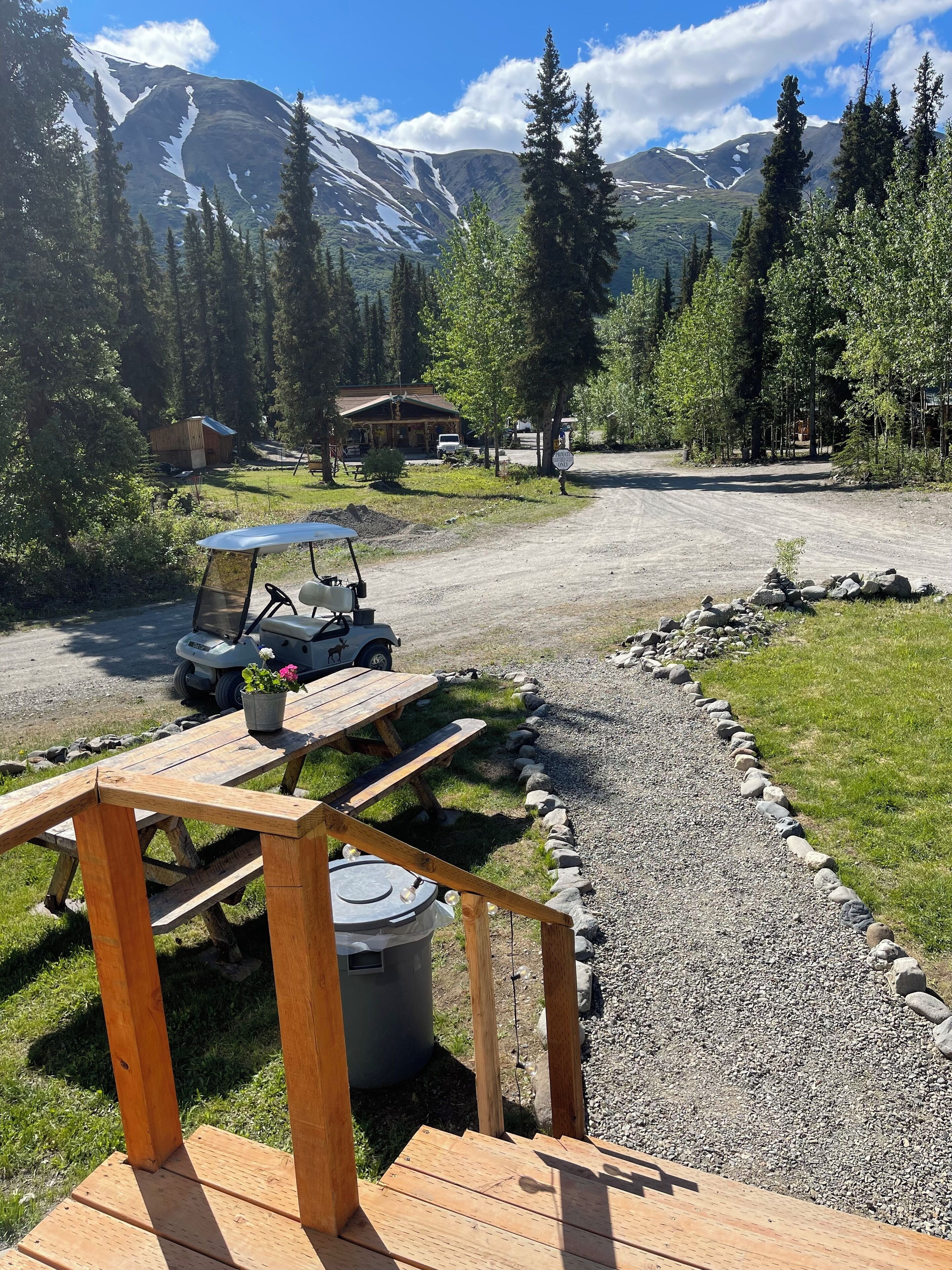 A wooden deck with picnic tables and a golf cart, surrounded by a gravel path and a stone border.