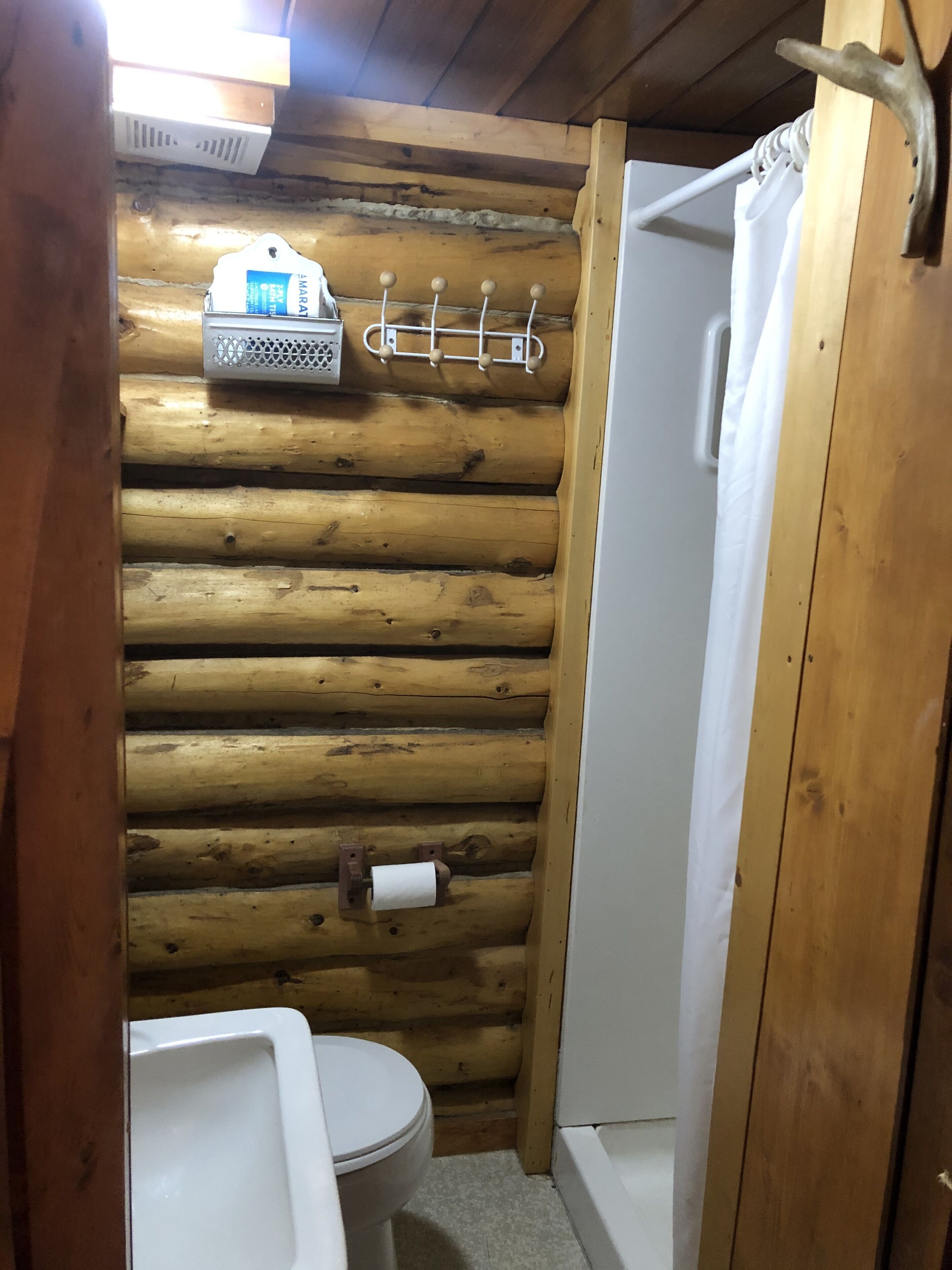 A wooden cabin bathroom with a toilet, sink, and shower.