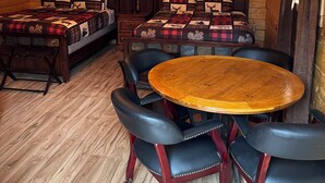 Una habitación tipo cabaña de troncos con dos camas, una mesa redonda de madera y sillas de cuero.