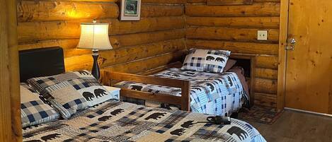 Une chambre dans un chalet en rondins, avec deux lits, un plafond en bois et un tableau encadré au mur.