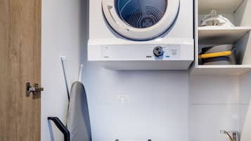 A compact laundry area with a front-loading washer and dryer, a small ironing board, and a sink.