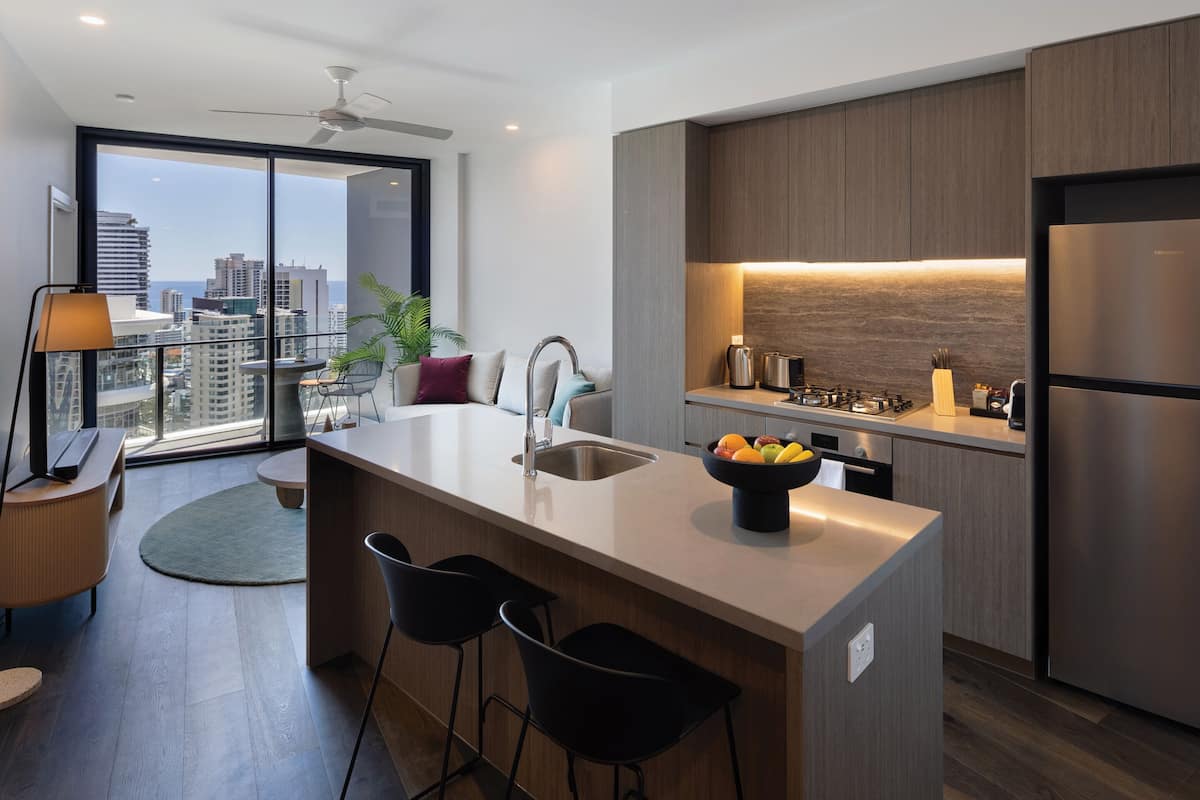 A modern kitchen with a central island, bar stools, a built-in sink, and a view of the city through large windows.