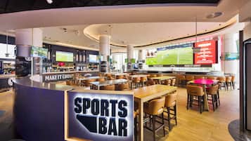 En sportbar med flera sittområden, en bardisk med en skylt som visar att det är en sportbar, och stora skärmar som visar sportevenemang.