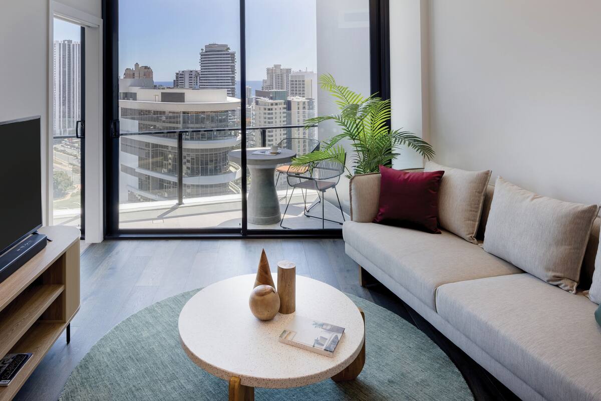 A modern living room with a large window, a round table, a sofa, and a TV.