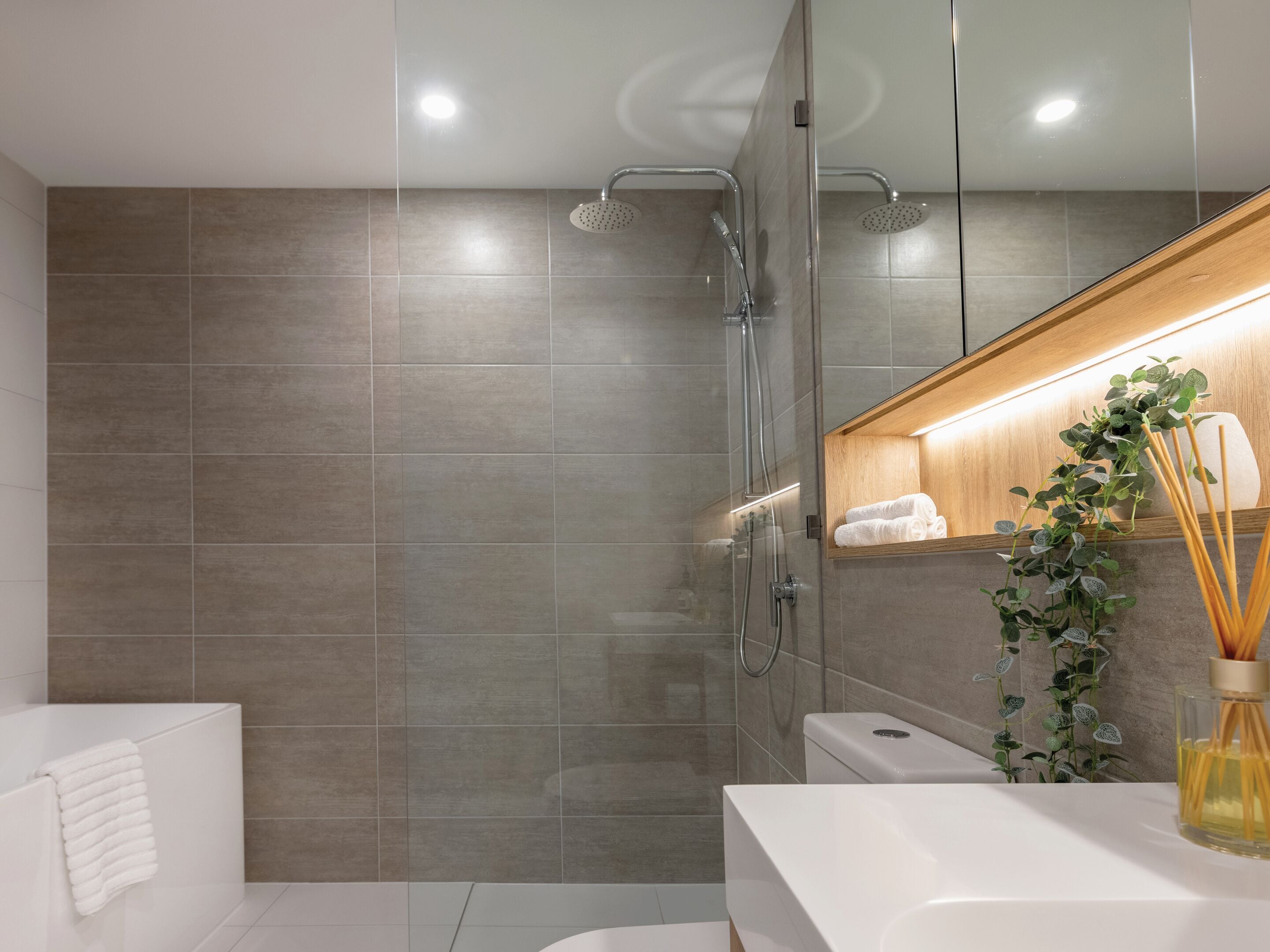 A modern bathroom with a glass shower enclosure, a white sink, and a wooden vanity.