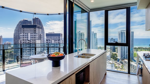 A modern kitchen with a large island, a bowl of fruit, and a city view through large windows. - The Star Residences Gold Coast (Broadbeach)