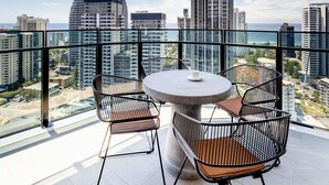 A balcony with a round table and four chairs, overlooking a cityscape with modern buildings and a clear sky. - The Star Residences Gold Coast (Broadbeach)