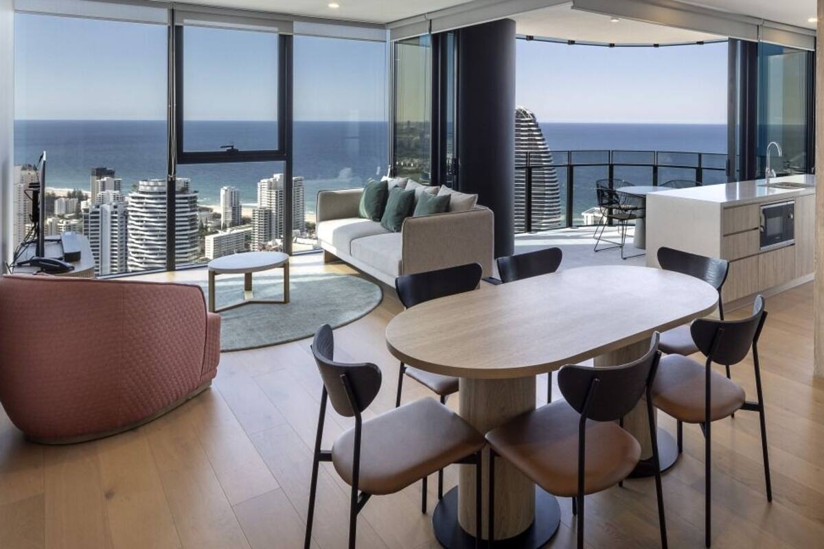 A modern living room with a large dining table, comfortable seating, and a view of the ocean and city skyline.