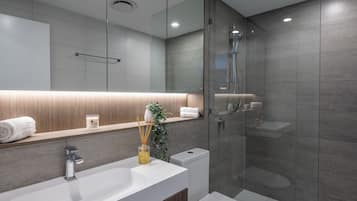 Un baño moderno con un espejo grande, un lavabo blanco, una cabina de ducha con mampara de vidrio y un inodoro.