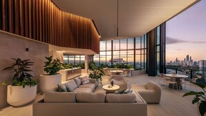 A modern rooftop lounge with a sofa, chairs, and a dining area, featuring large windows and potted plants. - The Star Residences Gold Coast (Broadbeach)