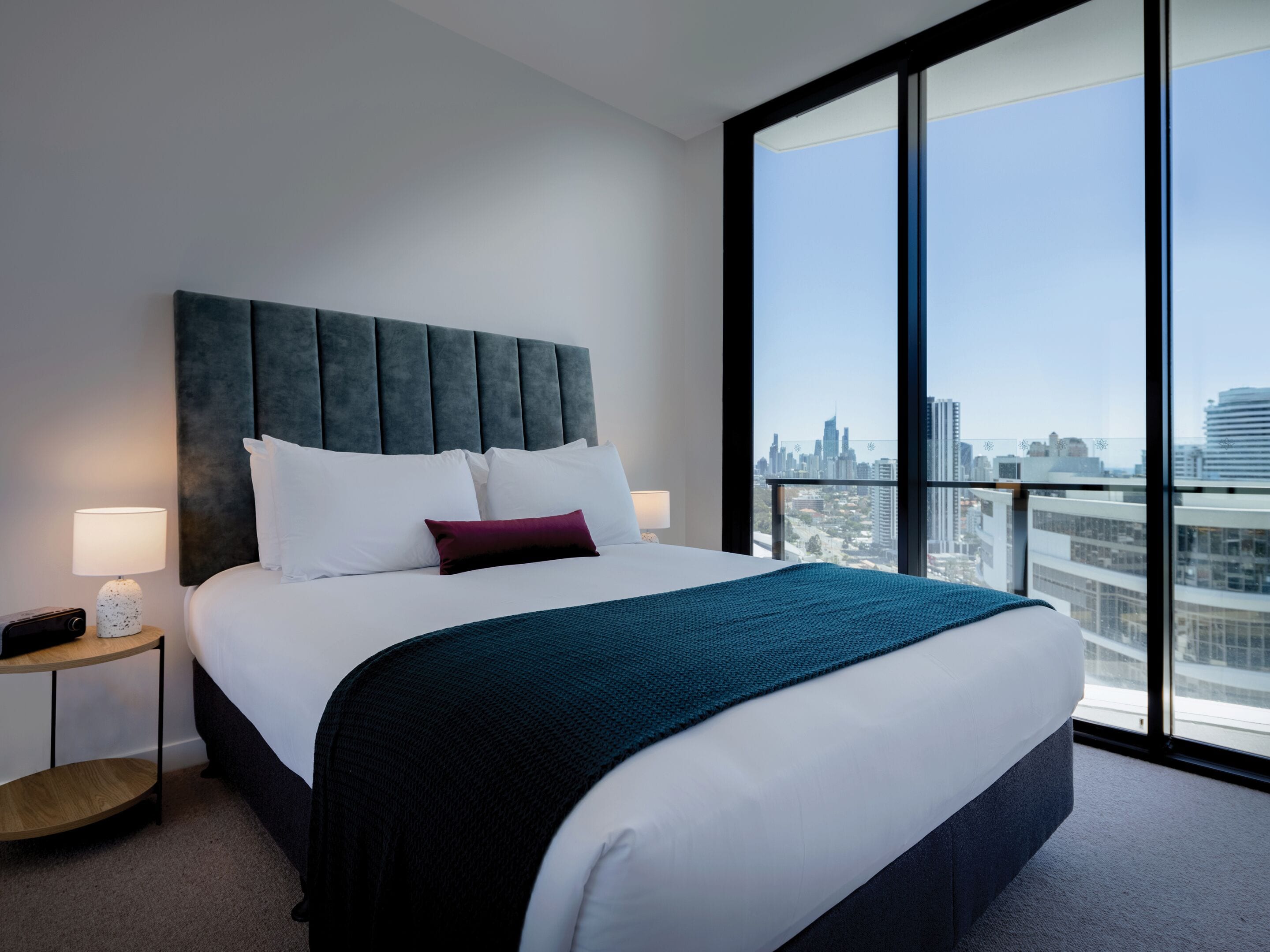 Camera d'albergo moderna con un ampio letto, vista sulla città e un tavolino rotondo in legno.