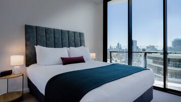 Camera d'albergo moderna con un ampio letto, vista sulla città e un tavolino rotondo in legno.