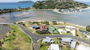 An aerial view of a coastal area with a road, a marina, and residential buildings. - Manaia Magic - Tairua Holiday Home (Tairua)