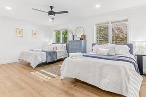 Ein Schlafzimmer mit zwei Betten, einem Deckenventilator, einer Kommode und großen Fenstern.
