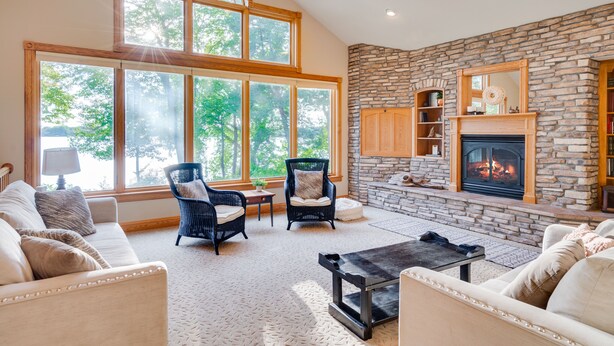 A spacious living room with a stone fireplace, large windows, and comfortable seating.