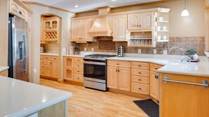 A modern kitchen with wooden cabinets, a stainless steel refrigerator, an oven, and a sink.