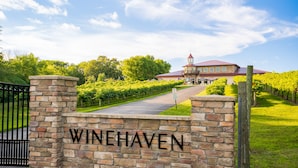 A stone wall with "WINEHAVEN" sign, a vineyard pathway, and a building with a red roof.