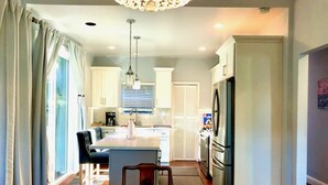 A modern kitchen with white cabinets, a central island, stainless steel appliances, and a chandelier.