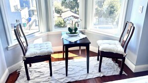 A corner room with two chairs, a table, and a view of a residential area through large windows.