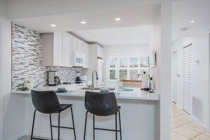 A modern kitchen with white cabinets, a tiled backsplash, and two bar stools.