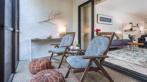 Un salon accueillant avec deux fauteuils en bois, un canapé et une table basse. Une branche décorative est fixée au mur, et une lampe se trouve sur une table d’appoint.