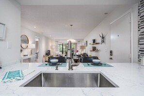 A modern kitchen with a central island, stainless steel sink, and a dining area in the background.
