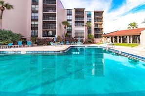 A hotel with a swimming pool, multiple balconies, and lounge chairs.