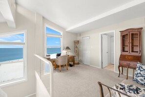 Ein geräumiges Zimmer mit großem Fenster und Meerblick, einem Schreibtisch mit Stuhl, einer Lampe und einem Holzschrank.