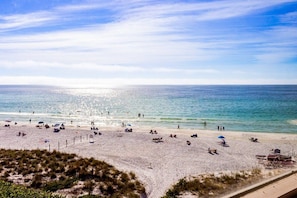 A beach with people sunbathing and swimming, a clear sky, and the ocean in the background.