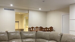 A living room with a beige leather sectional sofa, a dining table with chairs, and a white door. - GROUP CAMP ON MURRAY RIVER NEAR ECHUCA / MOAMA (Torrumbarry)